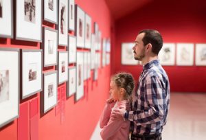 man and daughter at an art exhibit looking at prices